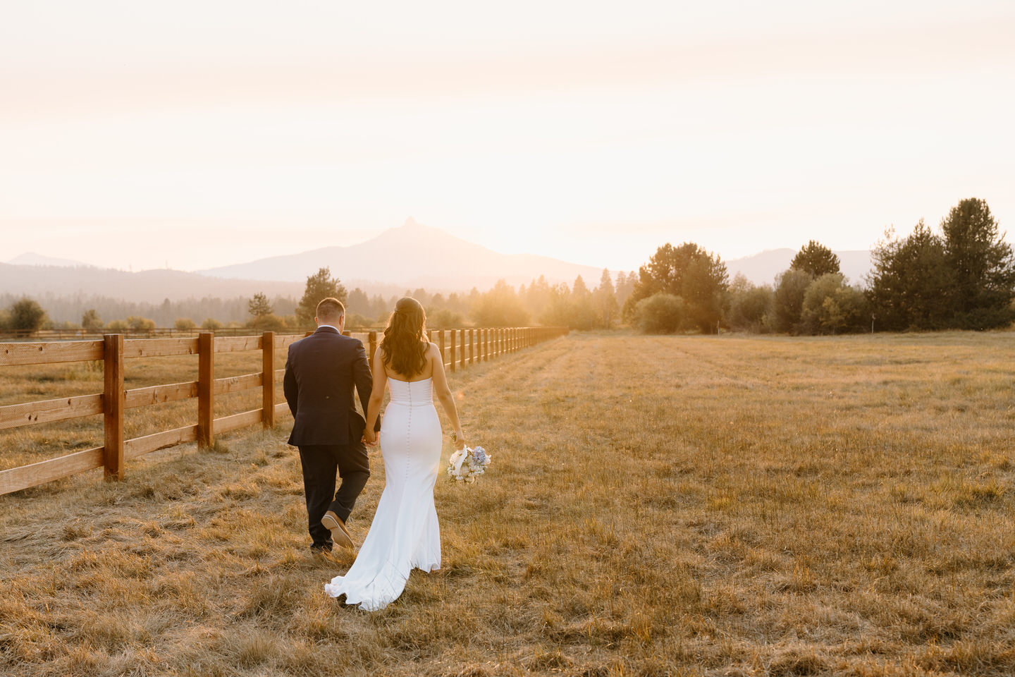 The bride and groom share a quiet moment at sunset, bathed in golden light and surrounded by a serene landscape.