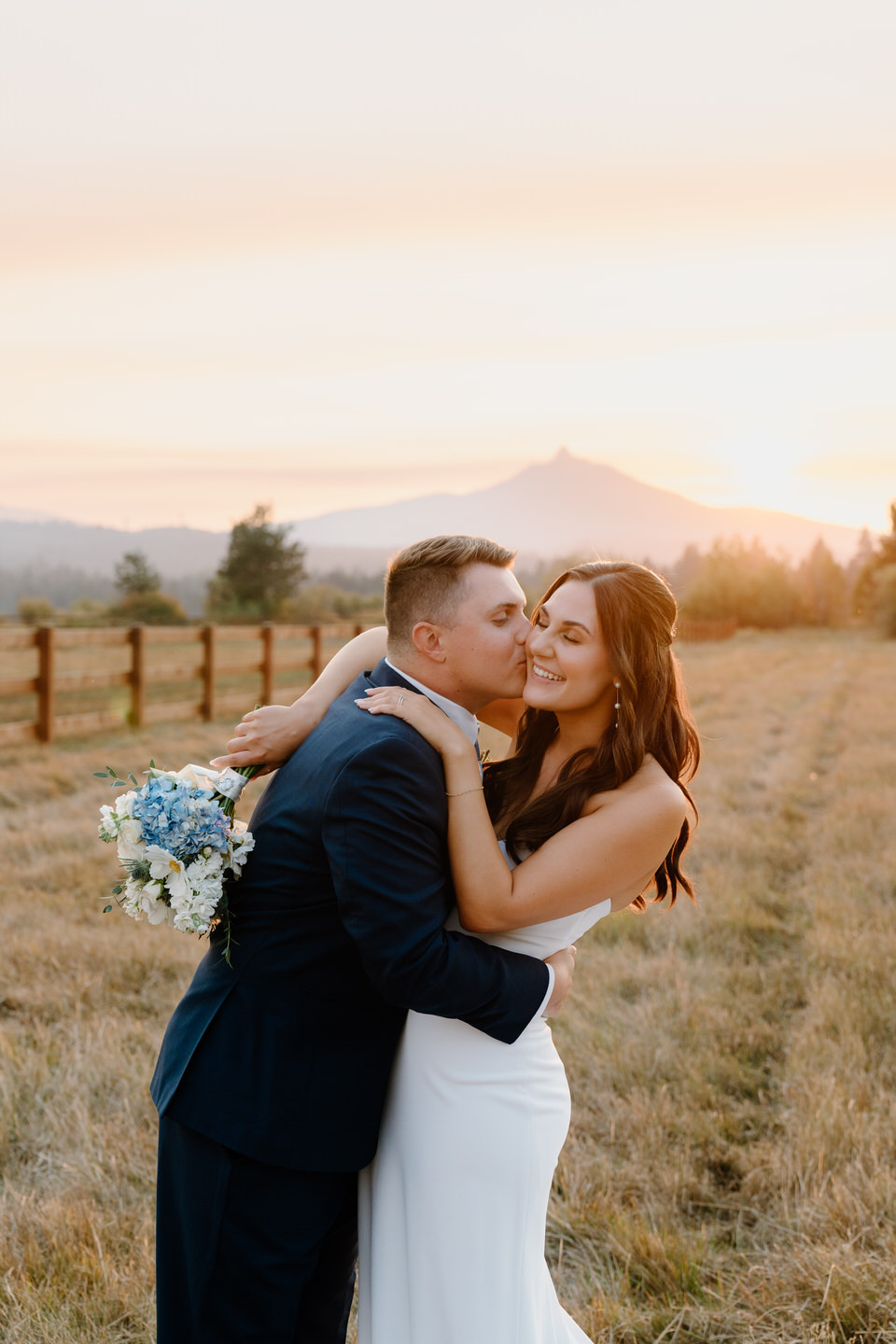 Bride and groom embrace at sunset, silhouetted against a glowing sky with warm golden hues.