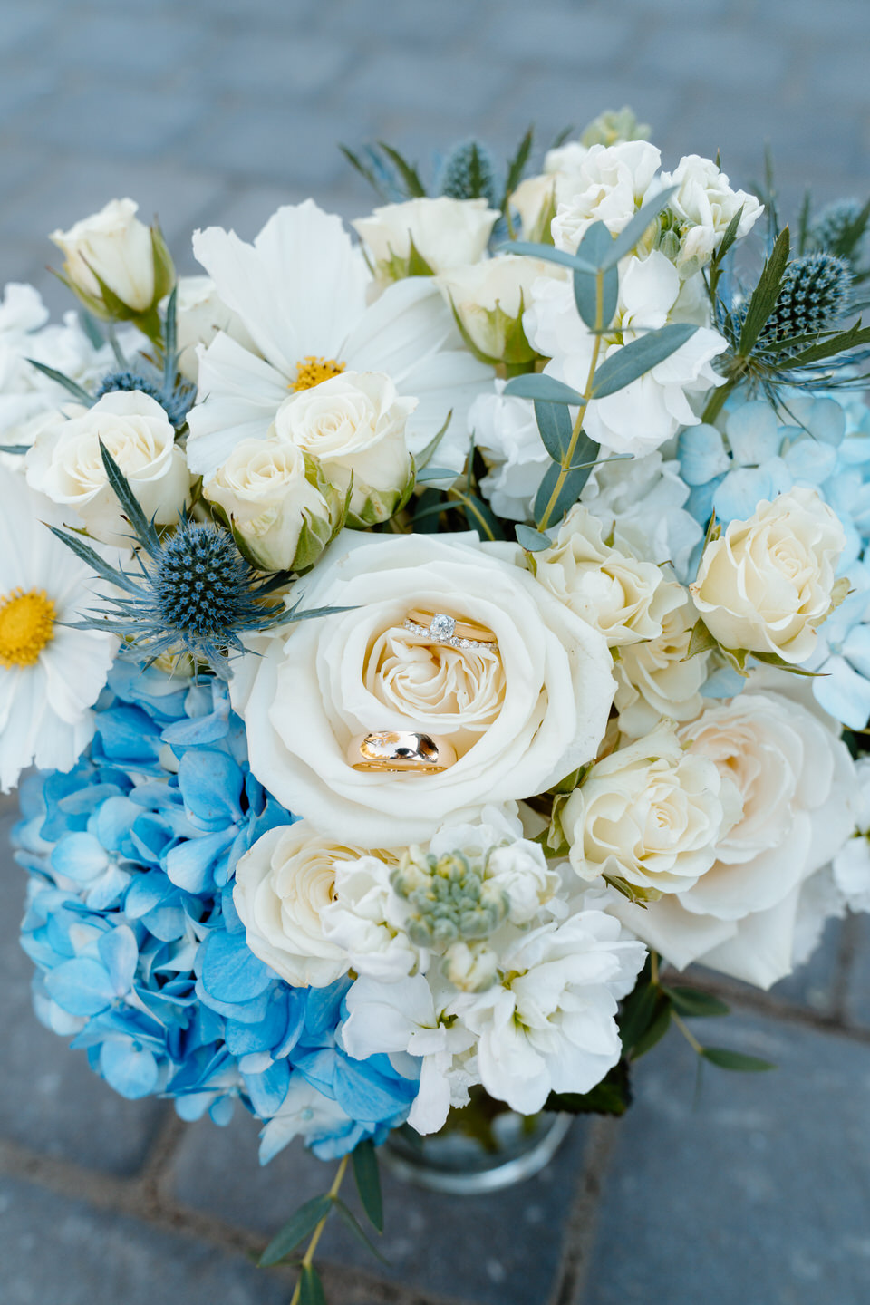 Bride and groom's wedding rings arranged inside of a cream rose in the center of the bride's wedding bouquet.