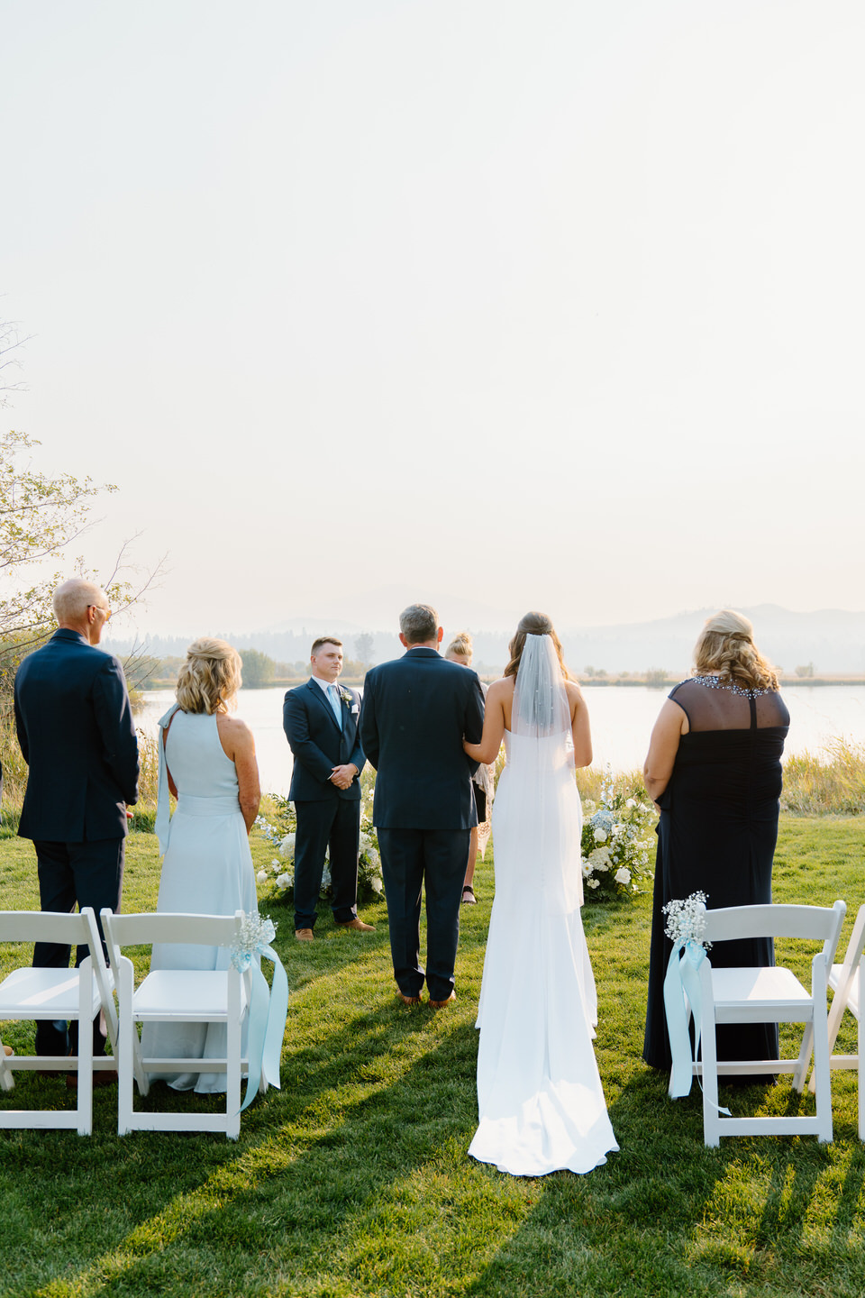 Father escorts the bride down the aisle at Black Butte Ranch, her dress flowing as they approach the groom under the open Central Oregon sky.