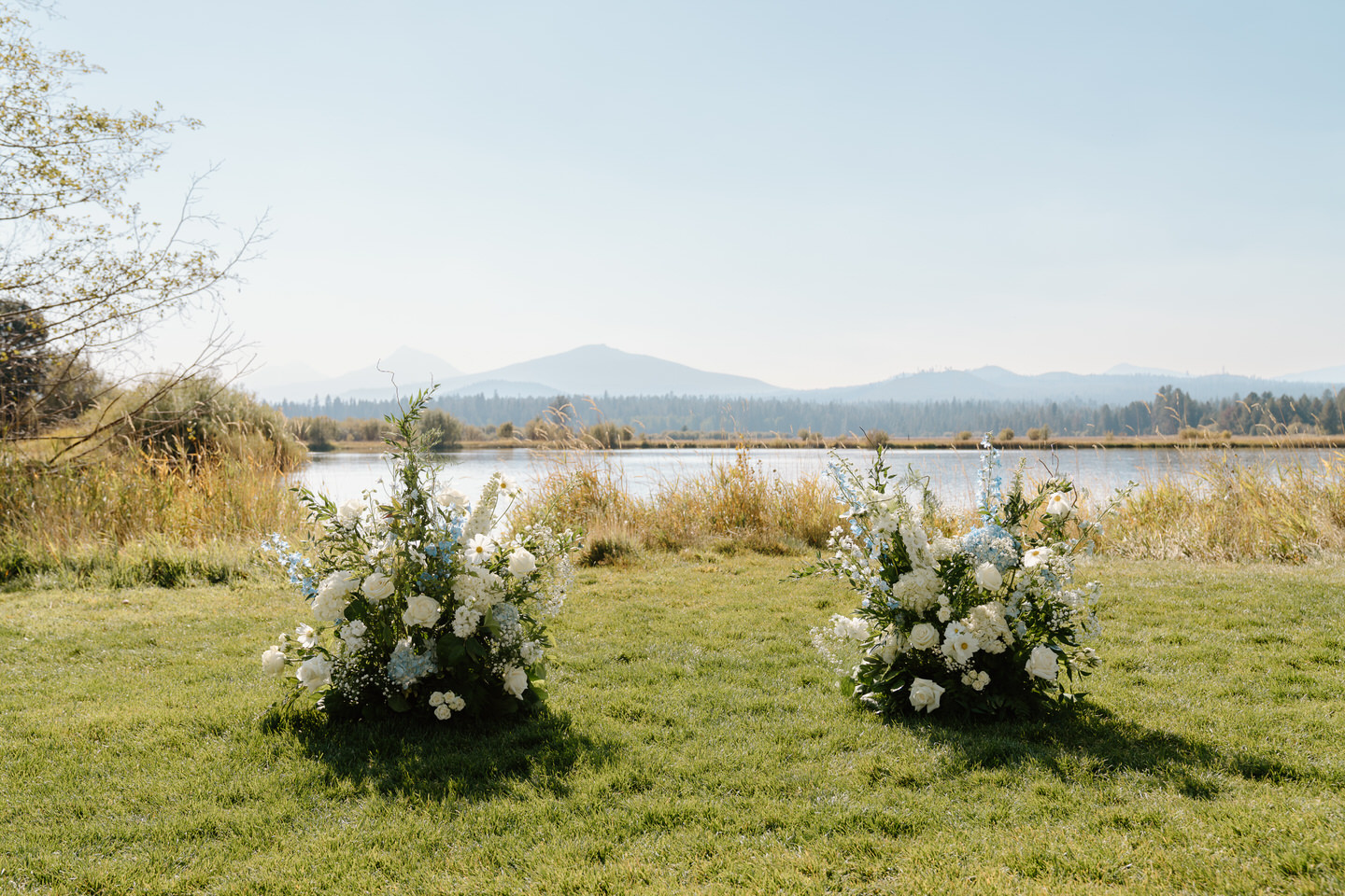 A blue floral installation rests on the ground in front of a serene lake at Black Butte Ranch, framed by Central Oregon's natural beauty.