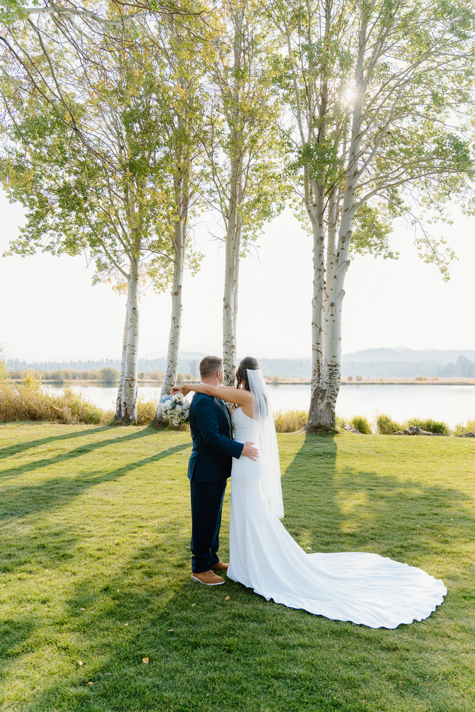 Bride and groom embrace as they look out over the lake and aspen trees of the Black Butte Ranch wedding venue.