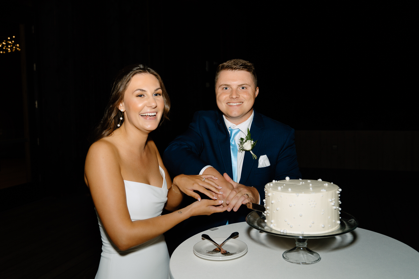 Bride laughing as she and the groom cut their simple, modern wedding cake with pearl accents.