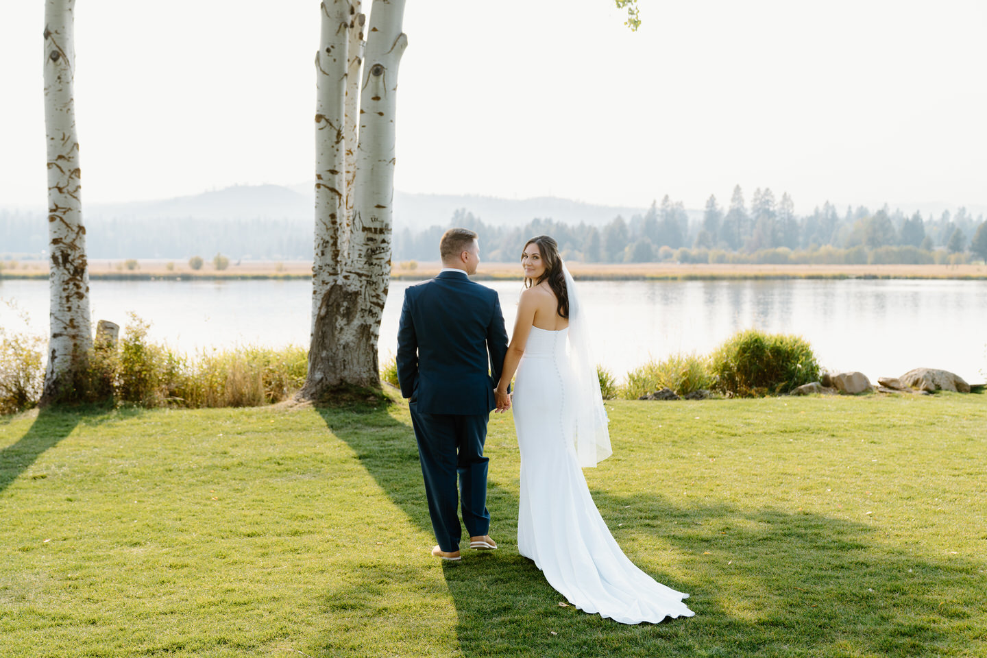 Bride and groom walk hand in hand near aspen trees, the lake of Black Butte Ranch reflecting the fall colors in the background.