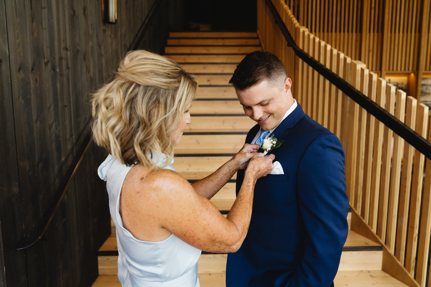 Smiling warmly, the groom’s mom adjusts his boutonniere, sharing a special moment at Black Butte Ranch on his wedding day.