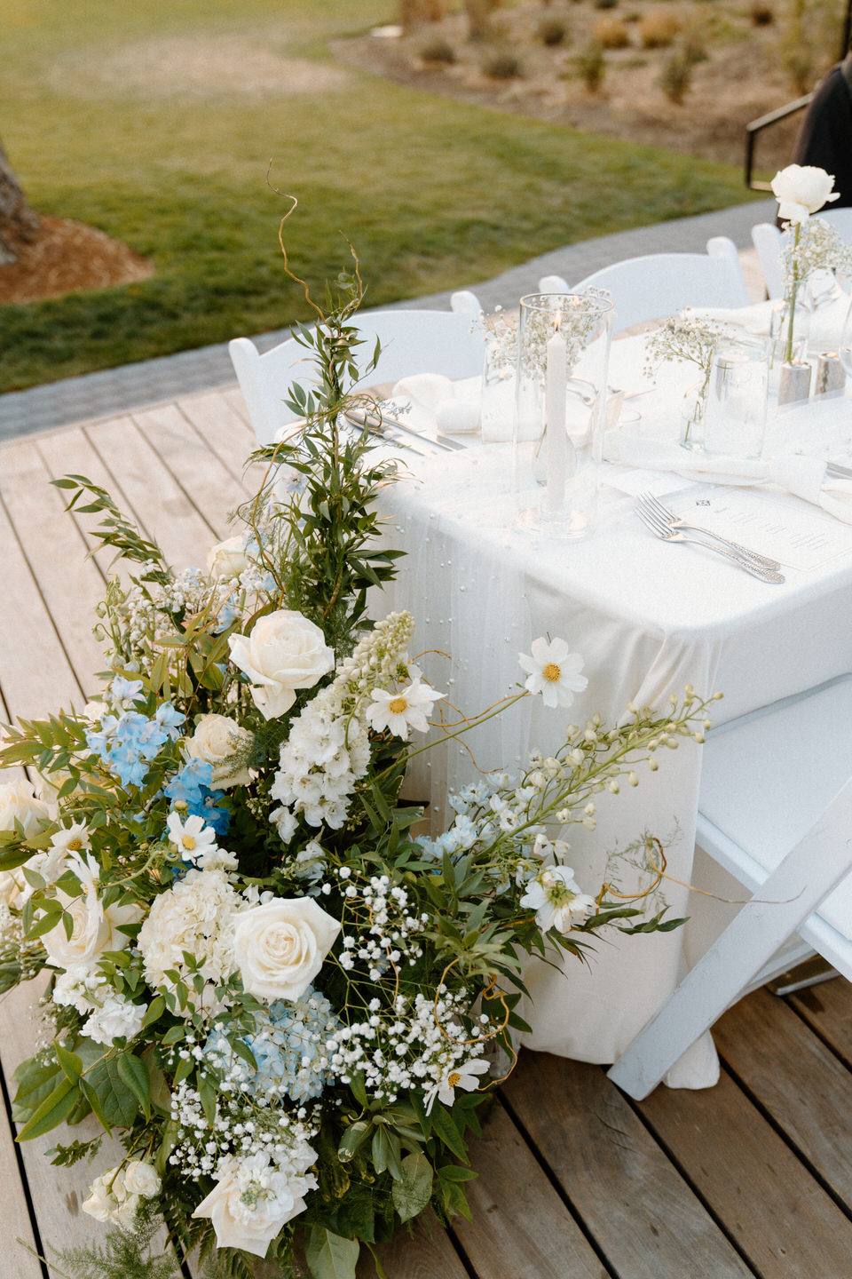 Elegant white table with minimal decor and a stunning floral installation of blue flowers on the ground in Black Butte, Oregon.