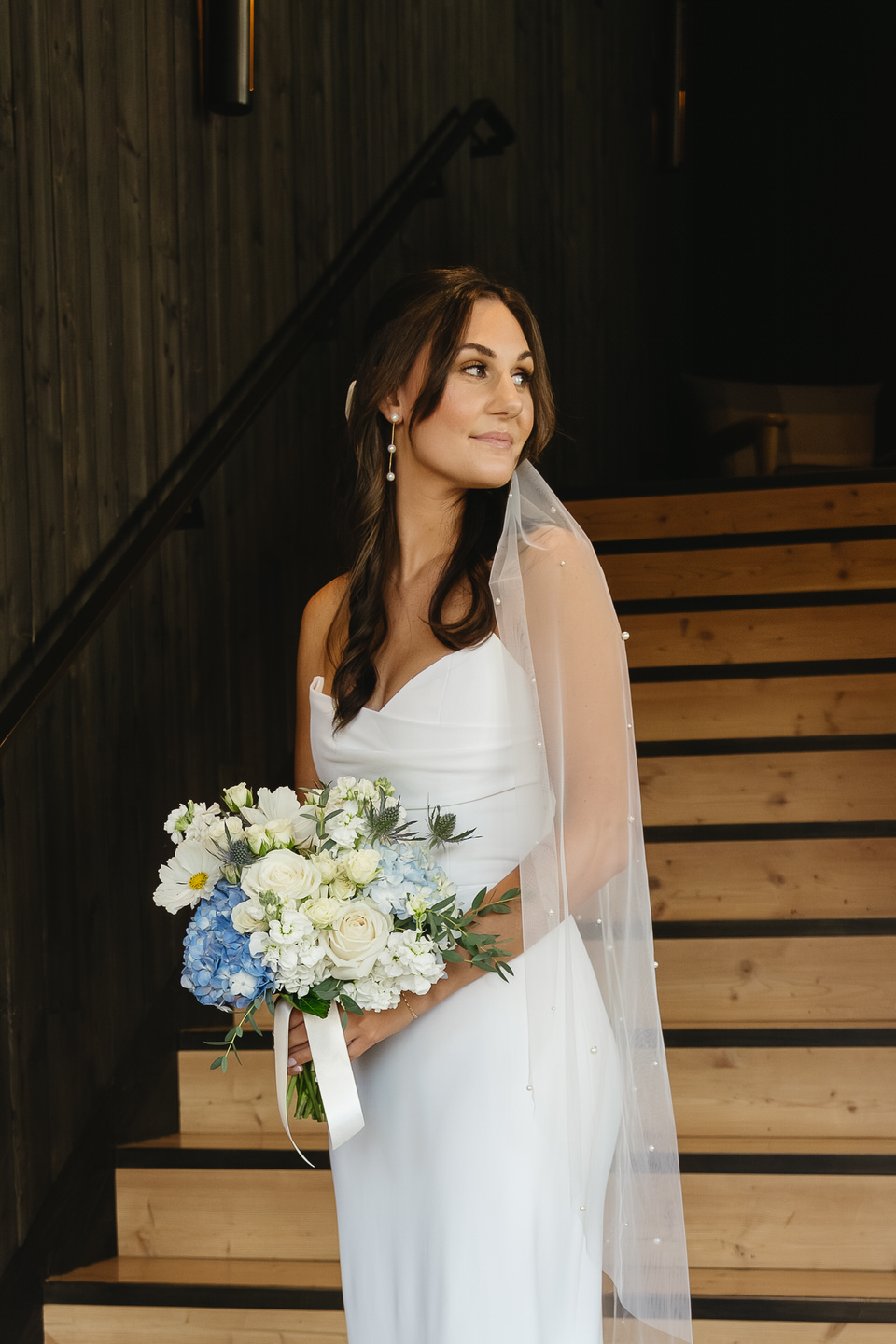 Bride gazes off to the side while standing on the majestic stairs of Black Butte Lodge, her dress flowing elegantly around her.