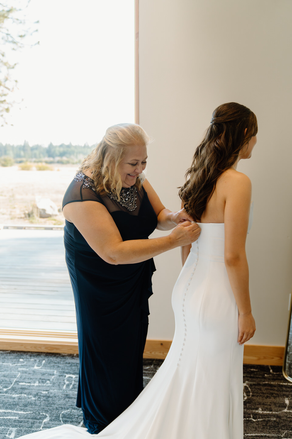 Bride and her mom sharing a tender moment as they button her into her Alyssa Kristen wedding gown.