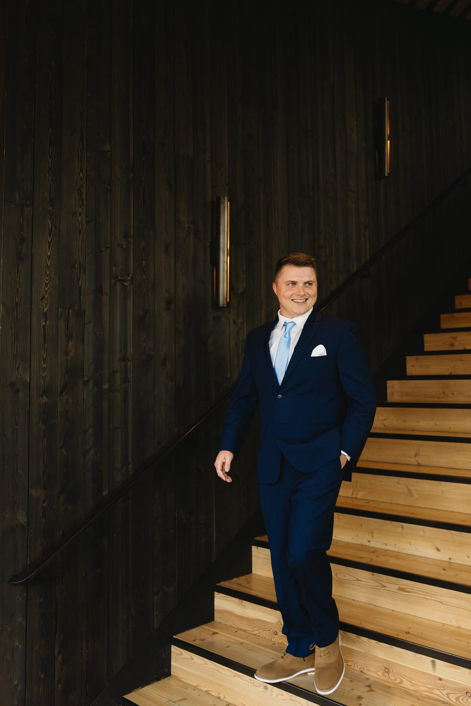 Groom in a blue suit stands confidently on the stairs of the Black Butte Ranch Lodge, exuding elegance and charm.