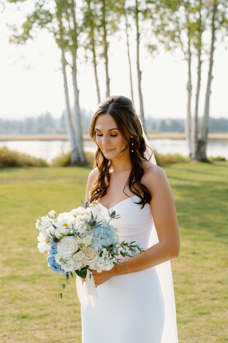 Bride looks down at her bouquet, softly smiling as she holds the whimsical arrangement in her hands at her Black Butte Ranch wedding.