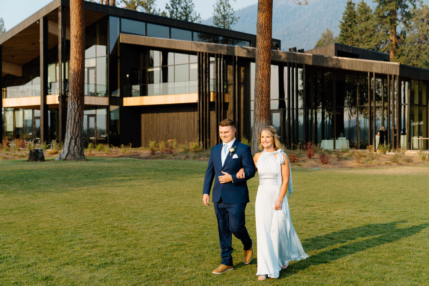 Groom and his mother walk down the aisle in front of the modern Black Butte Ranch lodge.