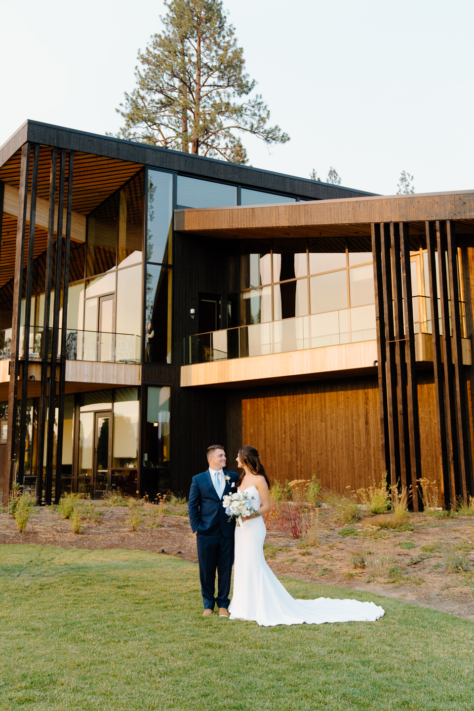 Bride and groom stand together in front of Black Butte Lodge, their elegant attire complimenting the lodge’s modern charm.