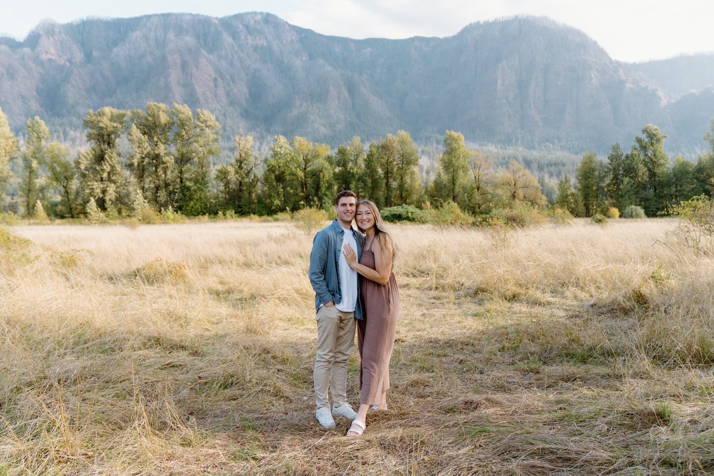 Newly engaged couple in a golden grass field with the cliffs of the Columbia River Gorge during their Oregon engagement photos.