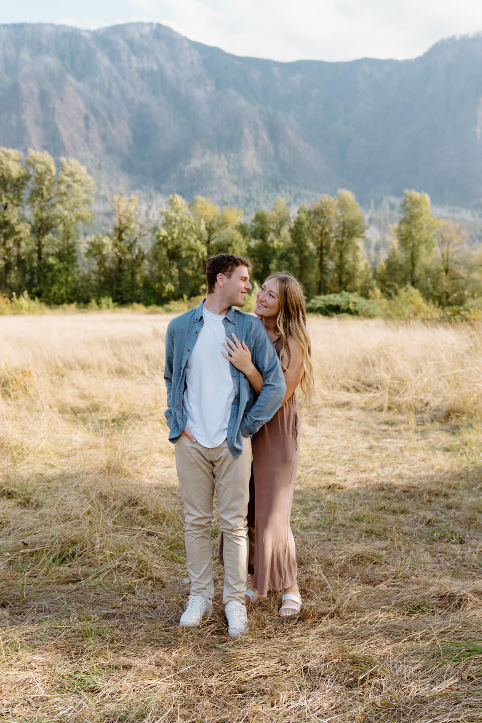 Romantic moment between a couple on a warm September day for their Oregon engagement photos, framed by dramatic cliffs and the greenery in the trees.