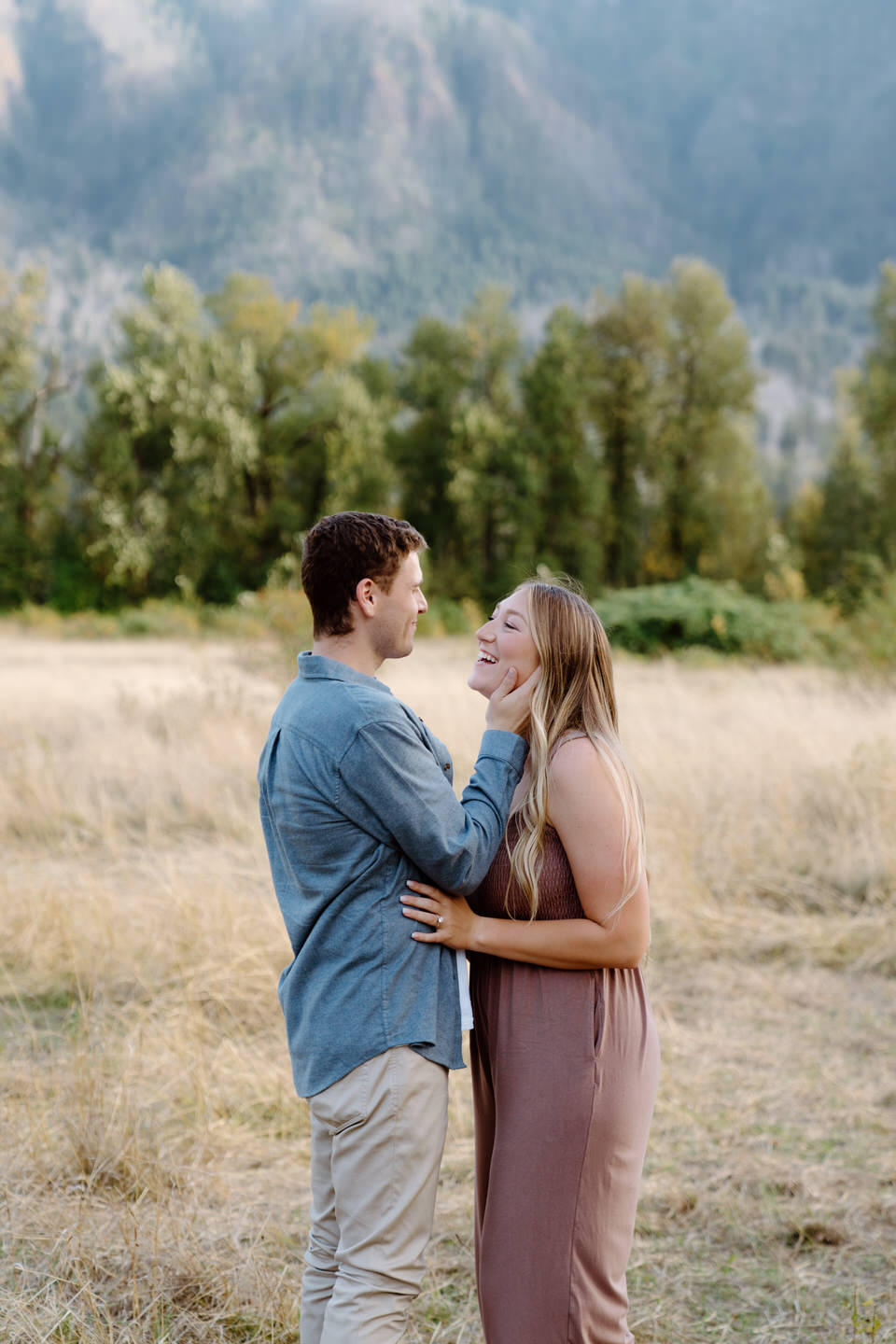 A fun photo of the couple looking into each other's eyes among a meadow for their Oregon engagement photos, surrounded by tall grass and distant cliffs.