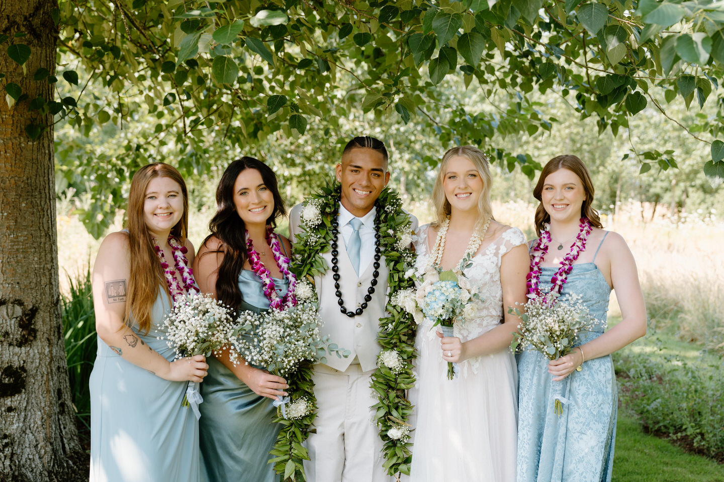 Wedding party poses together in front of the garden, celebrating the couple’s summer wedding at Green Villa Barn.