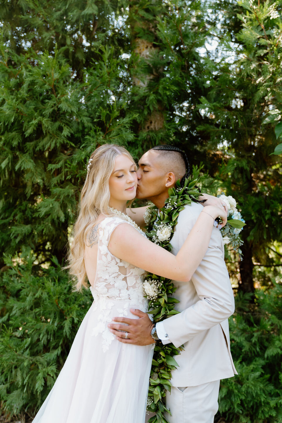 Bride and groom share a tender moment, the groom kissing the bride's cheek as they pose for portraits at their Oregon summer wedding.