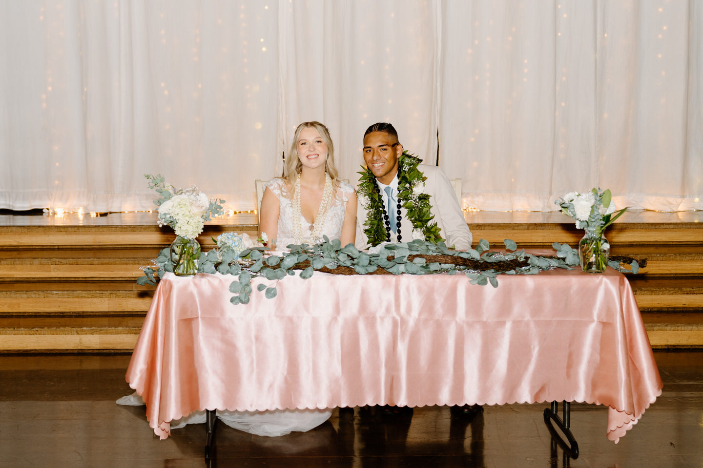 Bride and groom sit at their sweetheart table with pink wedding reception decor.