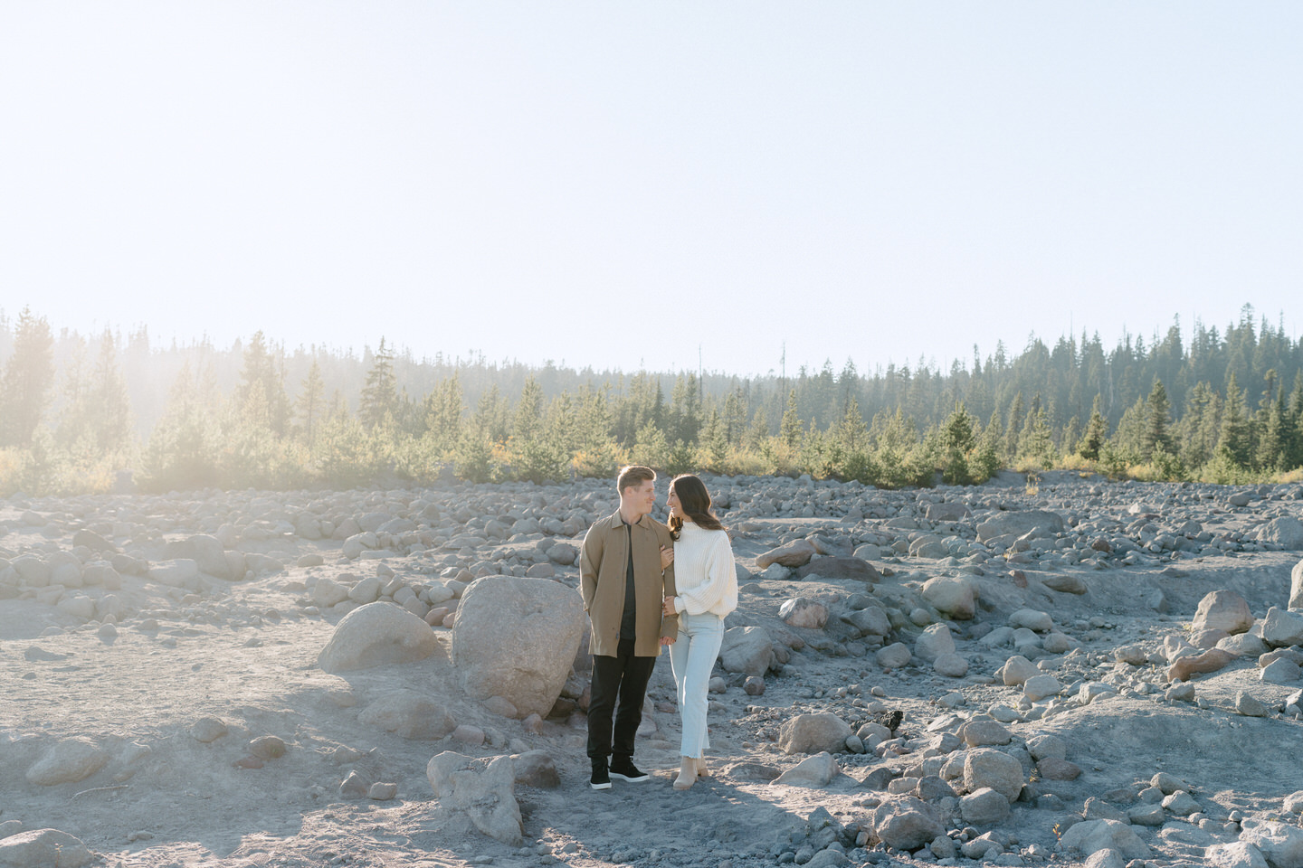 The couple standing side by side, gazing at Mount Hood in the distance, their cream and beige outfits complementing the subdued fall palette around them.