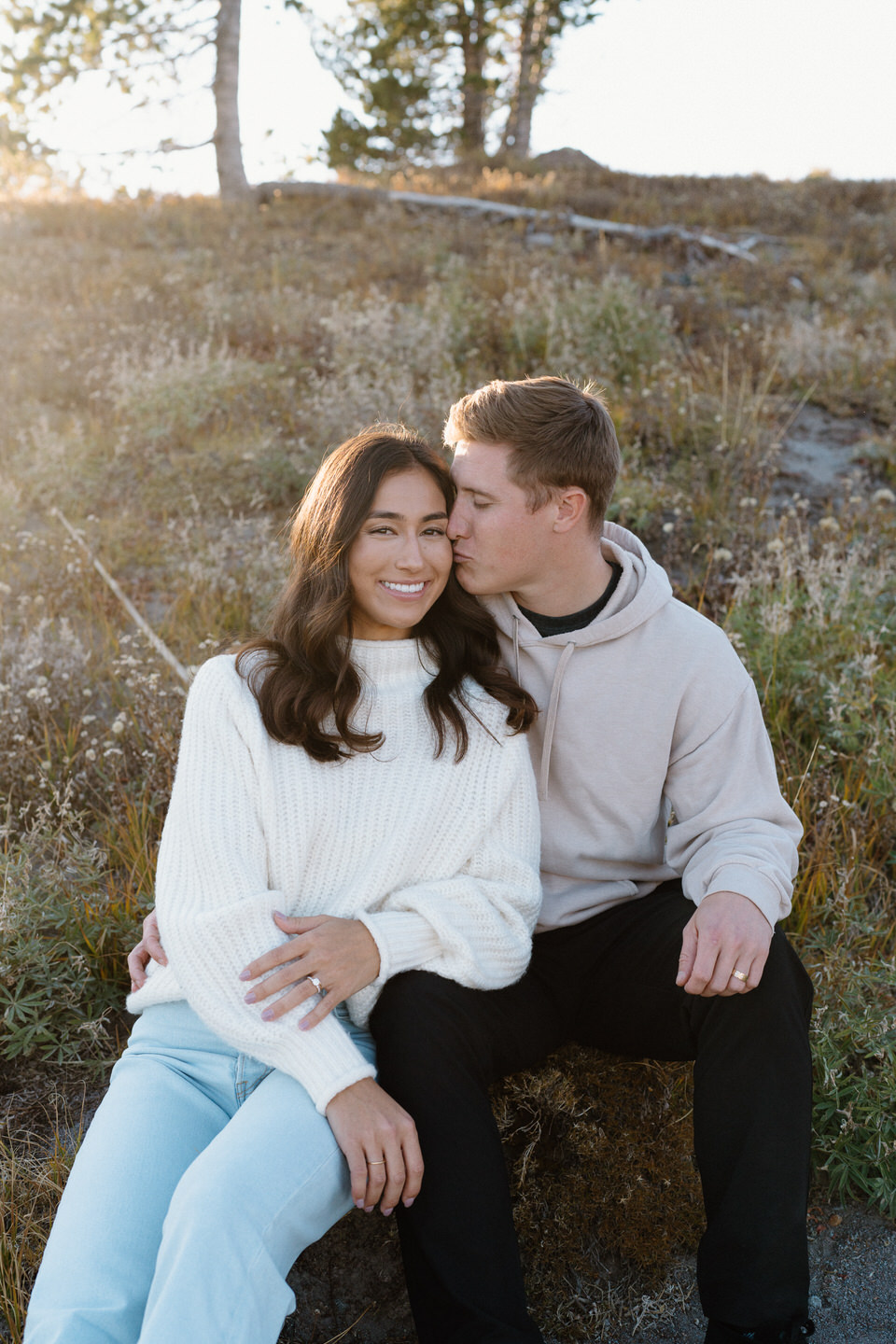 Couple sitting in fall foliage with golden light shining over the hill.