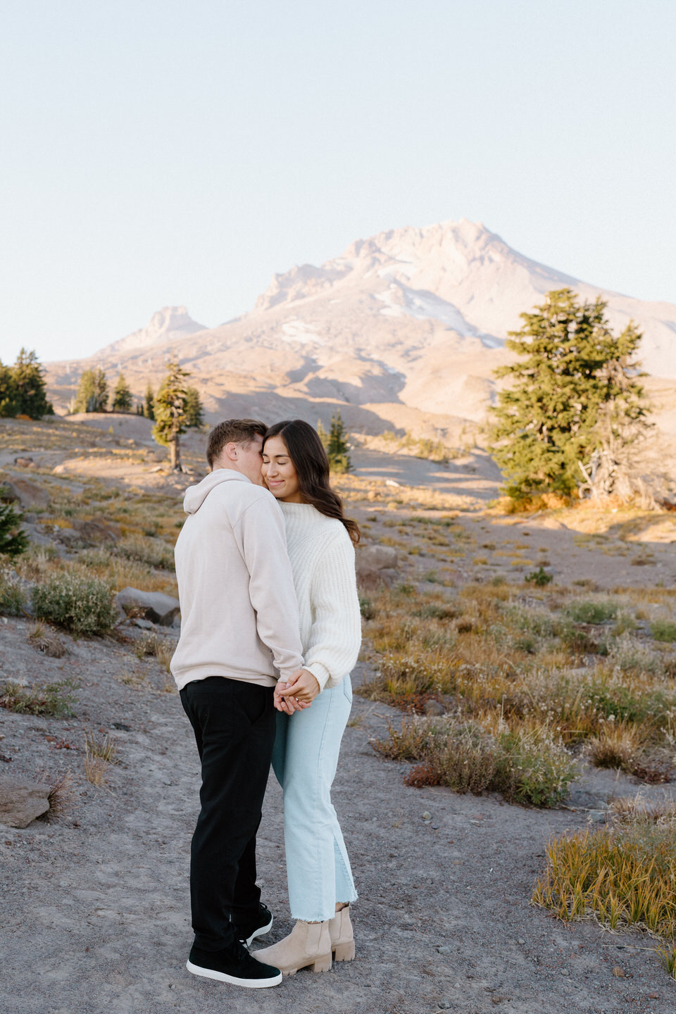 A warm embrace between the couple, their casual outfits blending with the muted tones of autumn at Mount Hood."