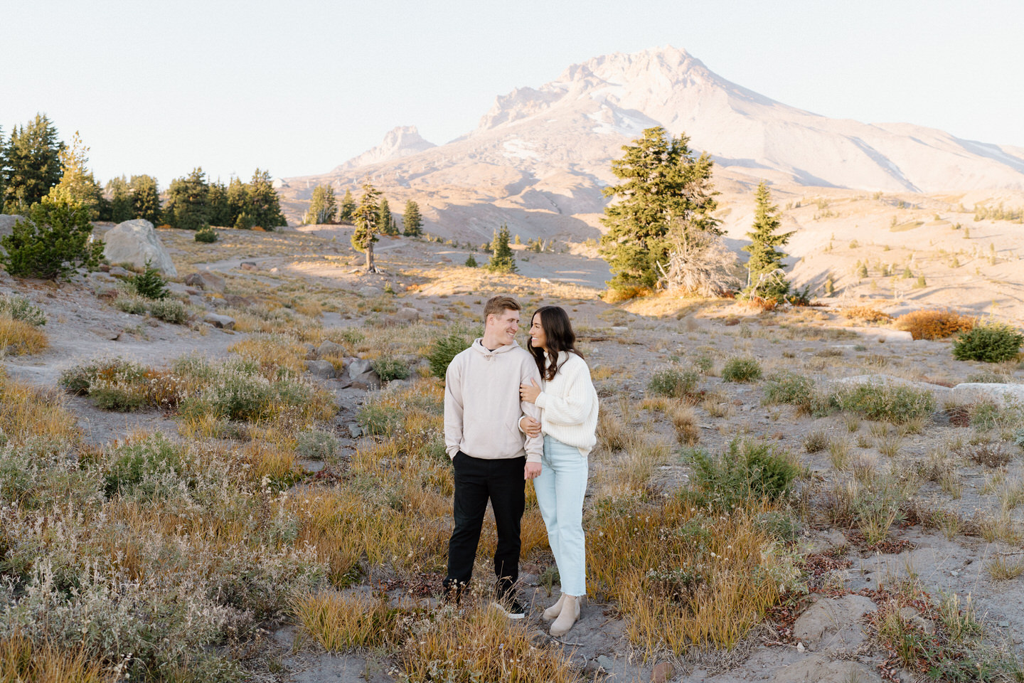 The couple leaning against each other, dressed casually, surrounded by fiery autumn hues on Mount Hood.