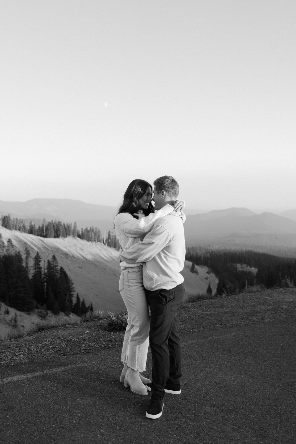 Black and white photo of a couple standing forehead to forehead in the Timberline Lodge parking lot.