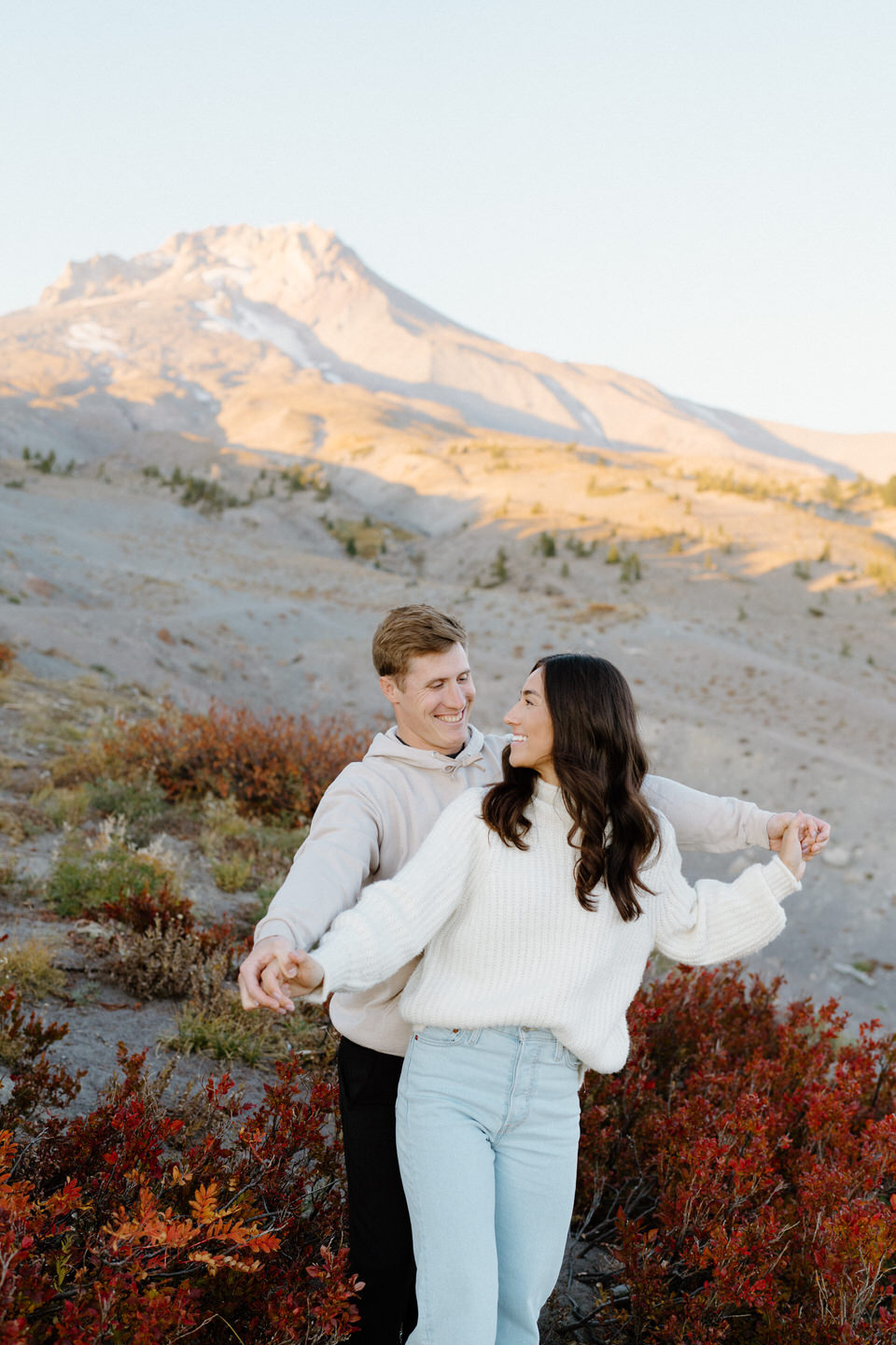 Couple in light colored outfits playfully dancing around in front of the fall foliage on Mount Hood.