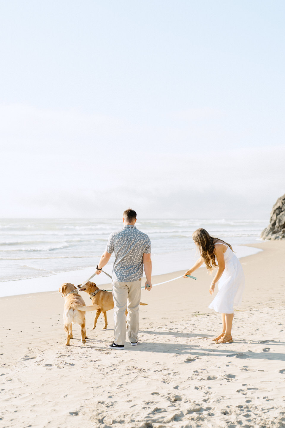 Engaged couple playing with two dogs on the beach at Oregon coast